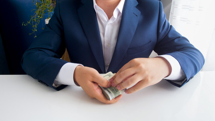 Closeup image of businessman in suit holding big stack of money