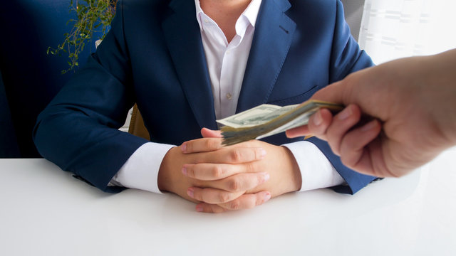 Closeup image of hand holding stack of money stretching towards businessman sitting in office