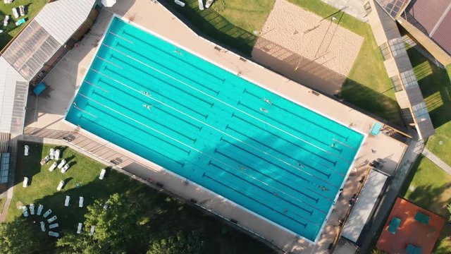 People Swimming and relaxing in Open pool at sunny day aerial vertical rolling shot