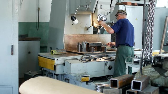 A man specializes a driller drilling holes on a drilling machine in a metal workpiece, a small business, private workshop, handmade driller