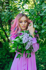 Obraz na płótnie Canvas Beautiful girl with colorful dyed hair and perfect makeup standig next to lilac bush