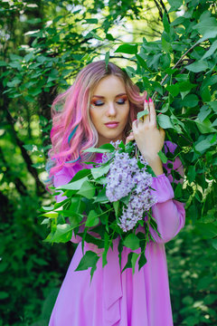 Beautiful girl with colorful dyed hair and perfect makeup standig next to lilac bush