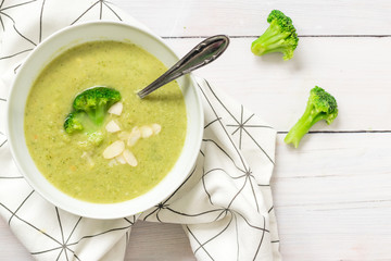 A bowl of soup with fresh broccoli on top, served on a white kitchen table, top view.