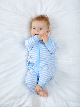 Charming blue-eyed baby 7 month old lying in bed in a striped bodysuit