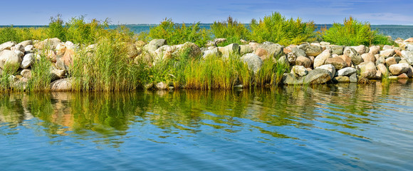 Seascape with island stones, grass and water reflection 