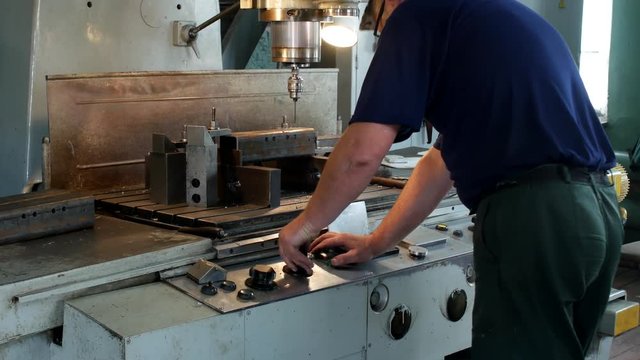 A man specializes a driller drilling holes on a drilling machine in a metal workpiece, a small business, private workshop