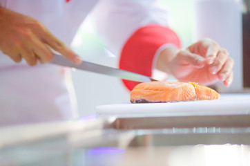 Chef cutting fresh salmon fillet in kitchen