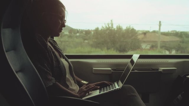 Young woman with glasses using laptop on moving train