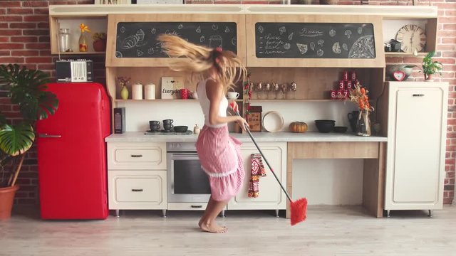 Young slim housewife washing the floor happily, good-looking woman walking along the well-furnished kitchen on saturday morning