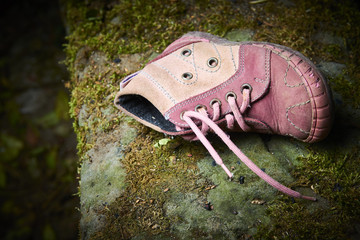 Abandoned baby shoe lying on an old stone covered with moss. Lost children's shoes.