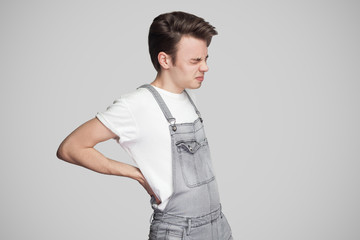 Portrait of unhappy illness teenager having strong backache, touching and pressing hands to back, closing eyes to relieve pain with helpless face. Isolated,studio shot,copy space on grey background