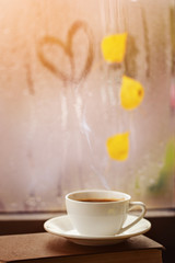 Cup of autumn tea (coffee, chocolate) and yellow leaves on rainy window, copy space. Hot drink for autumn mood.