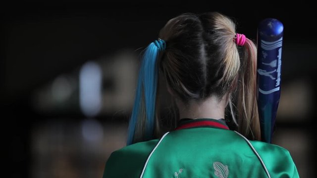 Unusual woman with fantastic makeup and unconventional hairstyle holding baseball-bat turning face