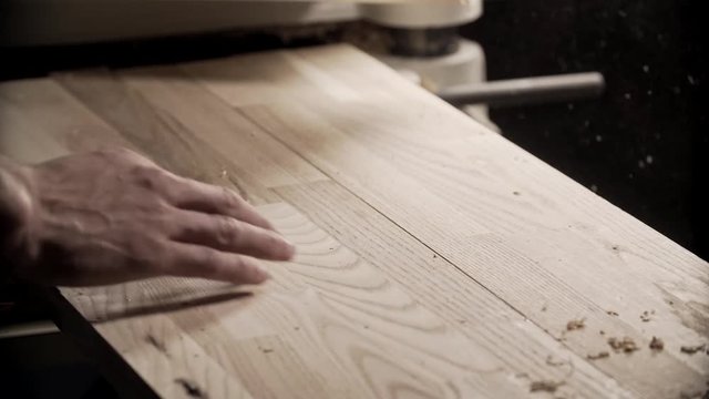 Carpenter hand touches wooden board. Master hand blows away dust from oak boardswiyh copy space at right