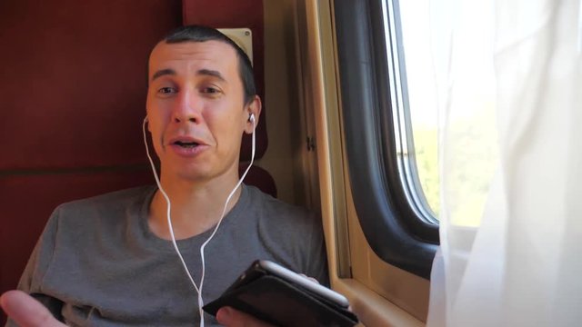 man listening to the music on the train rail car coupe compartment travel. slow motion video. man with a smartphone at the window of a train in a car travel internet social lifestyle media web. man