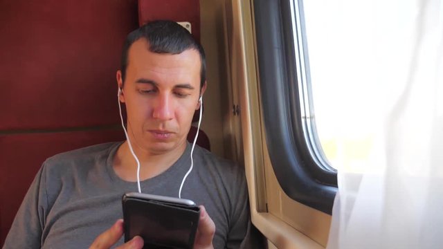 man listening to the music on the train journey rail car coupe compartment travel. slow motion video. man with a smartphone at the window of a train in a car travel internet social media web. man