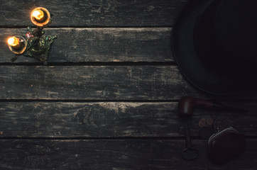 Bowler hat, rusty key, wallet with coins money, smoking pipe and burning candle on the wooden table background. Detective agent background.