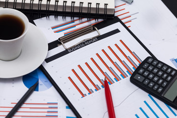 Business reports and cup of coffee. Blue graphs and charts and documents on black background. High angle view.