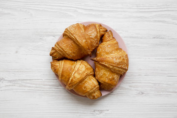 Fresh croissants with golden crust on white wooden table, overhead view. From above, flat lay.