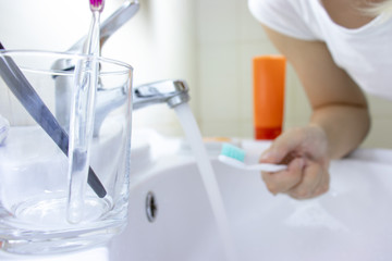 Clear glass with two toothbrushes in it, blurred woman with a toothbrush on background