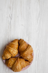 Fresh croissants on pink plate, top view. White wooden background. Overhead, from above, flat lay. Copy space.