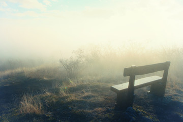 Wooden bench in a foggy forest. Artificial image with a vintage glamour glow filter.
