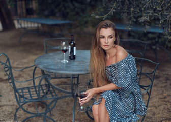 Fototapeta na wymiar Gorgeous girl drinking red wine sitting in a beautiful garden