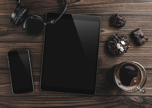 Top view of a tablet in high definition and technological devices, sweets and coffee on a wooden office table background