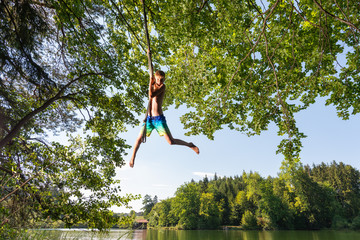 Boy swinging on tree rope next to wood lake
