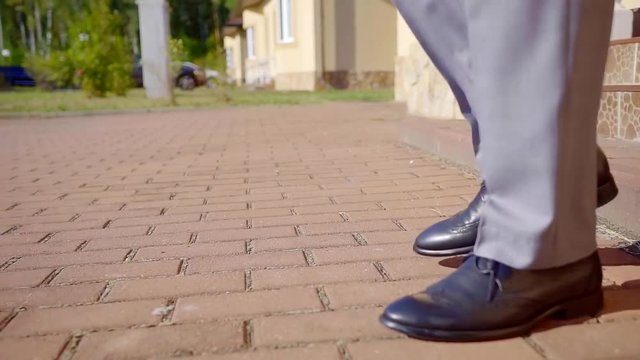 Close-up shot of a groom going to the wedding, black shiny shoes and grey suit.