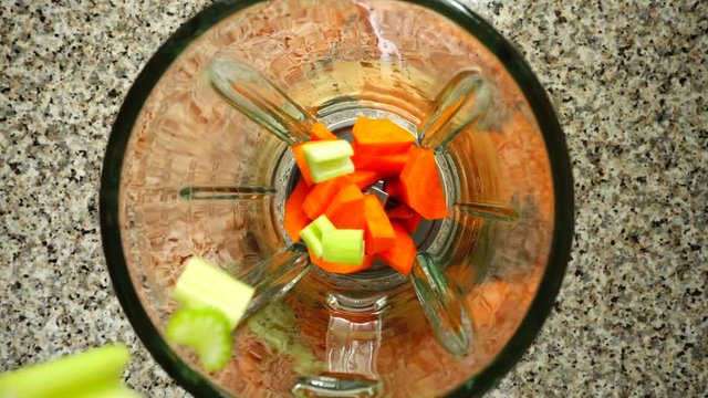 Stalk of an apium fall on carrots in a blender bowl. Slow motion.	Shooting in kitchen. Top view.	
