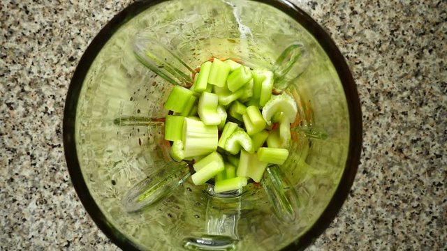Mentha leaves fall on stalk of an apium in a blender bowl. Slow motion.	Top view.