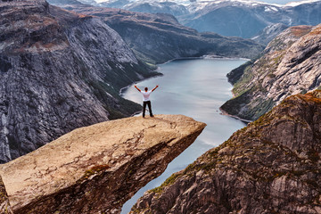 Tourist man standing in the Trolltunga and enjoys a beautiful view of the Norwegian fjord.