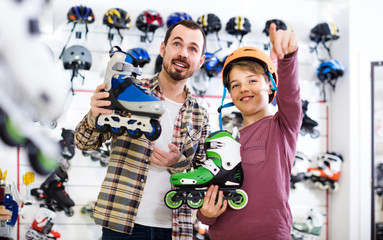 Male shop assistant helping boy to choose roller-skates in sports store