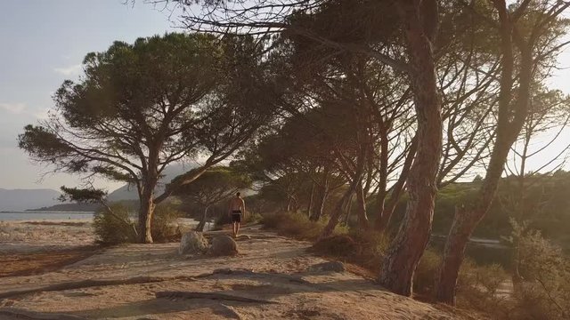 Young man walking through the trees at Cala Osalla beach, Sardinia, Italy. Mediterranean coast, with sandy beach and green vegetation. Concept of travel, tourism, holiday, exploration, trip, nature.