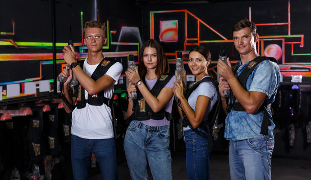 Portrait of positive young friends standing with laser guns during laser tag game