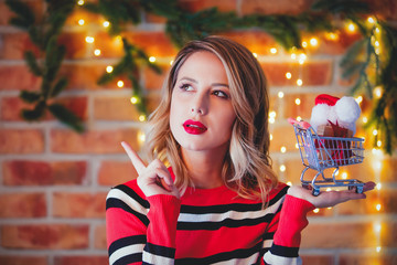 Portrait of a young girl in red striped sweater with gifts and cart at Christmas lights background