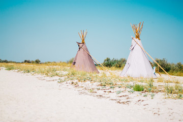 Wigwams on the sandy seashore. Indian native national building outdoors summer. Teepees on coast. © baklykovadaria