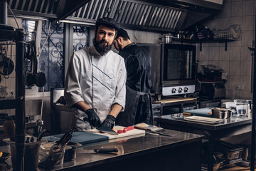 Obraz na płótnie Canvas Two brutal cooks dressed in uniforms preparing sushi in a kitchen.