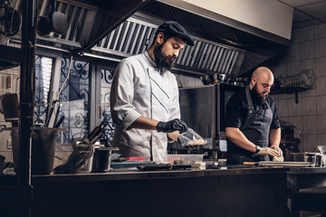 Fototapeta na wymiar Two brutal cooks dressed in uniforms preparing sushi in a kitchen.