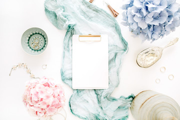 Blank paper clipboard, turquoise blanket, colorful pastel hydrangea flower bouquet, woman fashion accessories on white background. Flat lay, top view mock up.