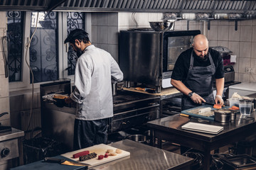 Two brutal cooks dressed in uniforms preparing sushi in a kitchen.