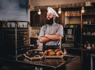 Bearded chef in uniform showing tray of fresh bread in the kitchen of the bakery.