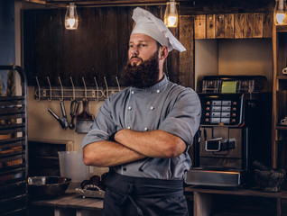 Professional baker in cook uniform posing with crossed arms near in bakery.