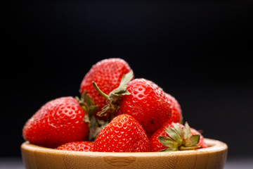 Photo close-up of ripe strawberry in wooden cup on black background