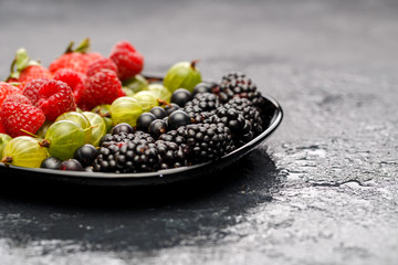 Photo of blackberry, strawberry, raspberry, gooseberry on black plate