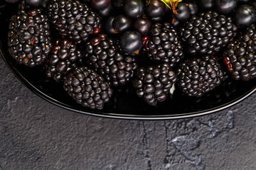 Photo on top of blackberries, black currant on black plate on black empty background
