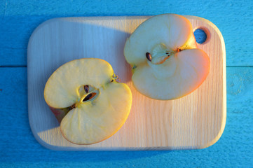 apple cuted in half on a wooden board on turquoise table with a long blue shadow