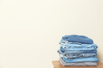 Stack of different jeans on table against light background. Space for text