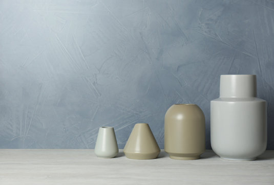 Beautiful ceramic vases on table against color wall. Space for text